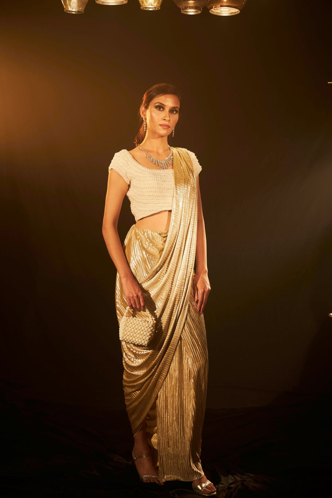 Saia metallic slit saree with an embellished pearl blouse will definitely make you look sassy and elegant in an event.  Tailored to perfection in a metallic fabric, the saree features a slit from the waist level and has an attached palla which creates a great fall.  It comes with a pearl embellished blouse with cap sleeves and deep from the back.