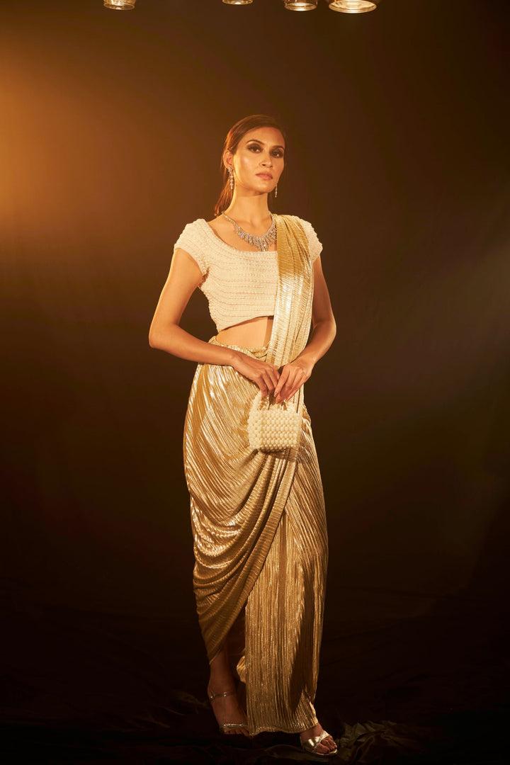 Saia metallic slit saree with an embellished pearl blouse will definitely make you look sassy and elegant in an event.  Tailored to perfection in a metallic fabric, the saree features a slit from the waist level and has an attached palla which creates a great fall.  It comes with a pearl embellished blouse with cap sleeves and deep from the back.