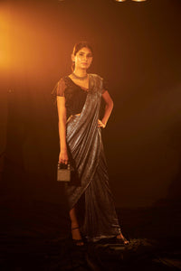 Saia metallic slit saree with an embellished pearl blouse will definitely make you look sassy and elegant in an event.  Tailored to perfection in a metallic fabric, the saree features a slit from the waist level and has an attached palla which creates a great fall.  It comes with a pearl embellished blouse with a deep V-neckline and ruffle sleeves in organza and deep from the back.